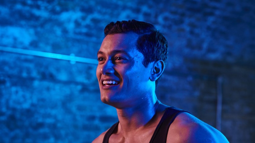 Head and shoulders shot of a man running in a tunnel, lit up by blue neon lights