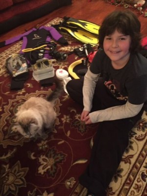Ben sitting on a carpet with a cat and scuba gear.